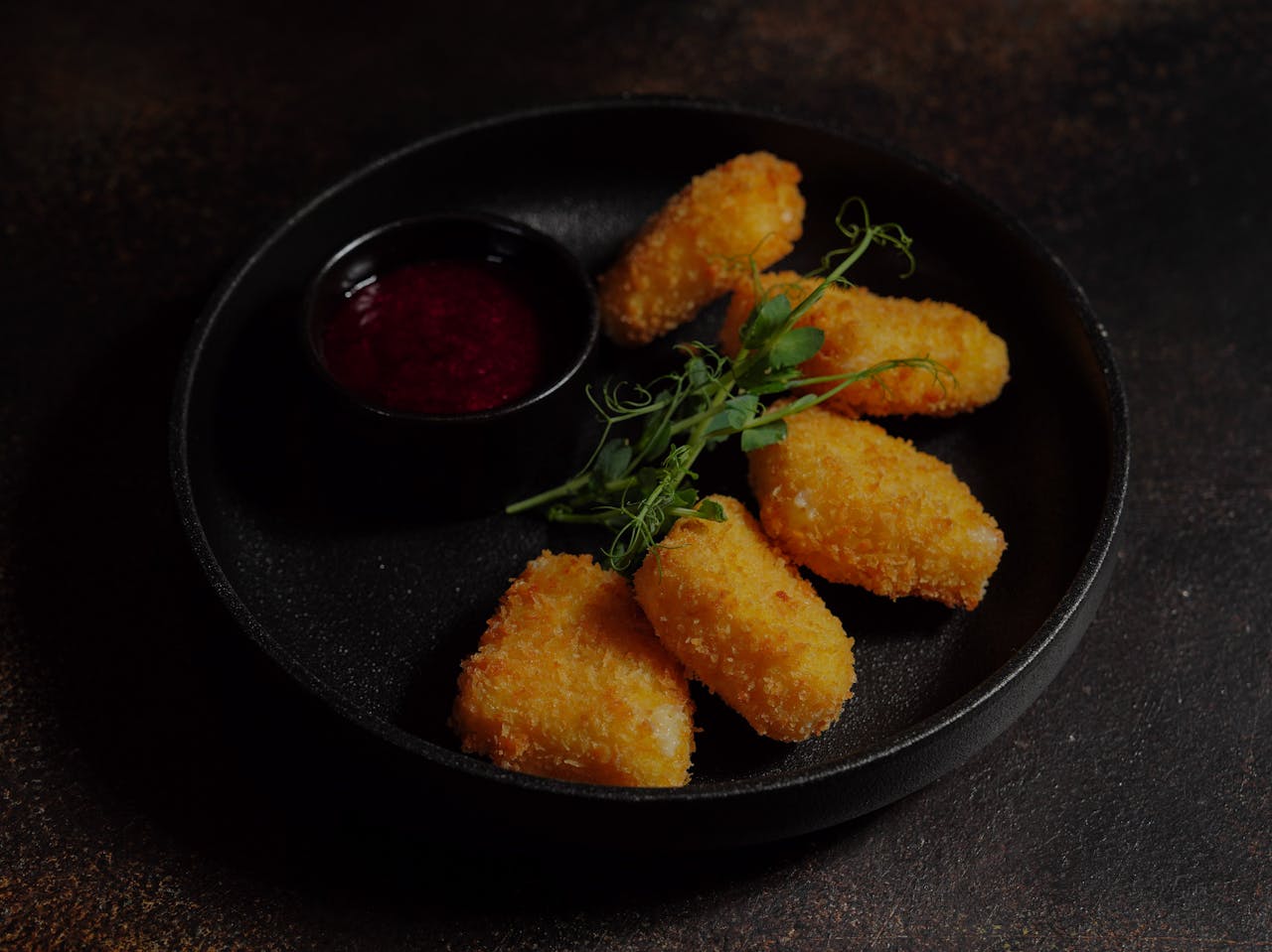 Delicious crispy chicken nuggets served with a tangy dipping sauce on a black plate.
