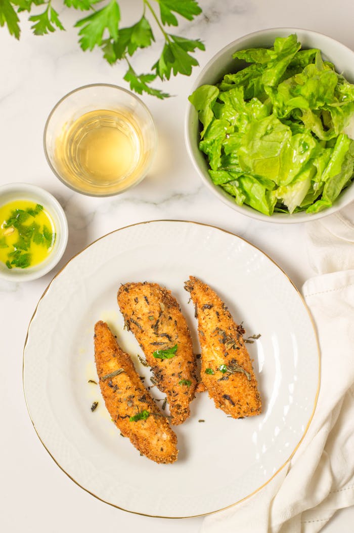 Top view of herb-crusted chicken served with fresh lettuce salad and a glass of white wine.
