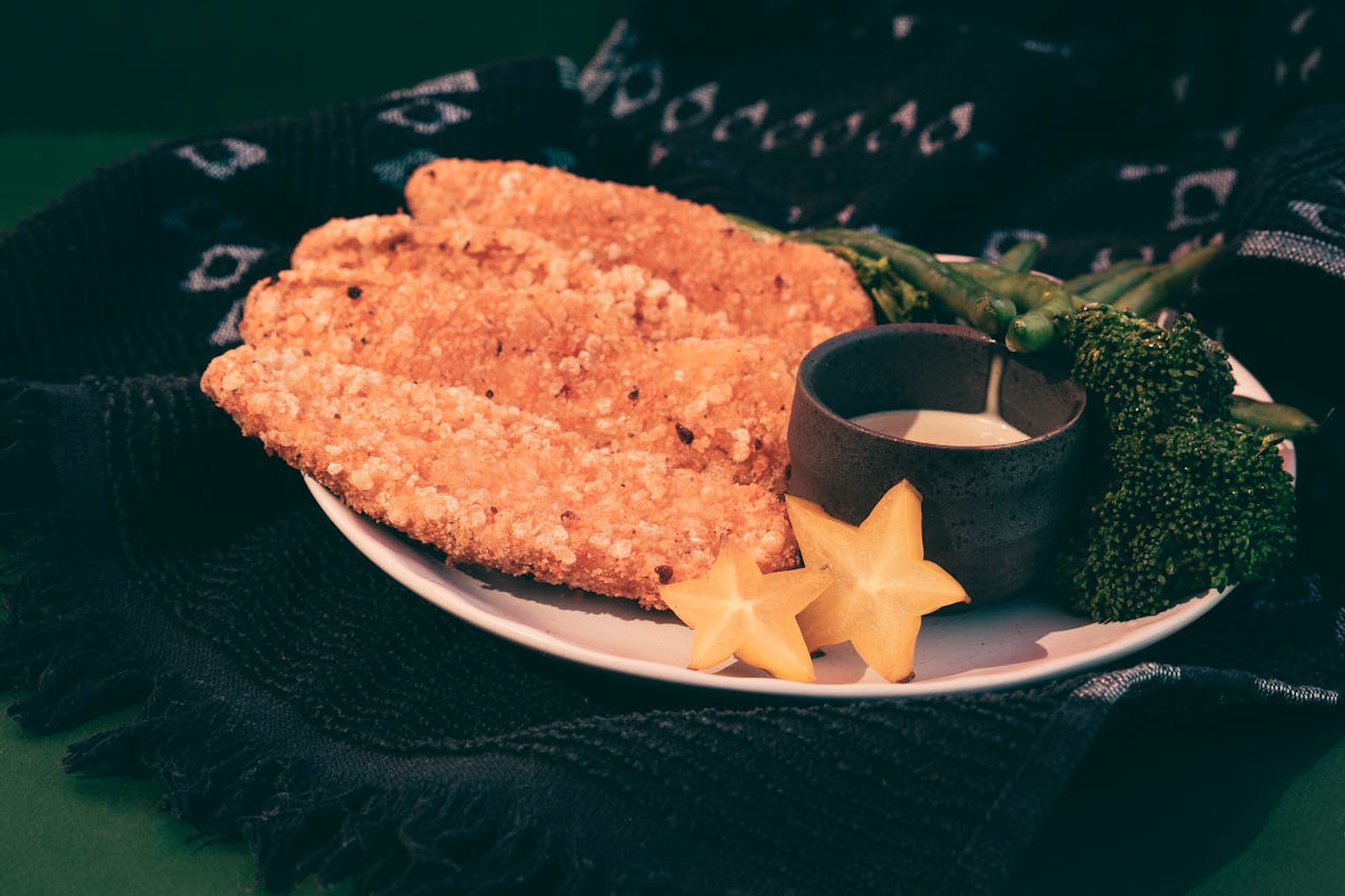 A delicious plate of crispy chicken served with broccoli and starfruit, garnished with sauce.