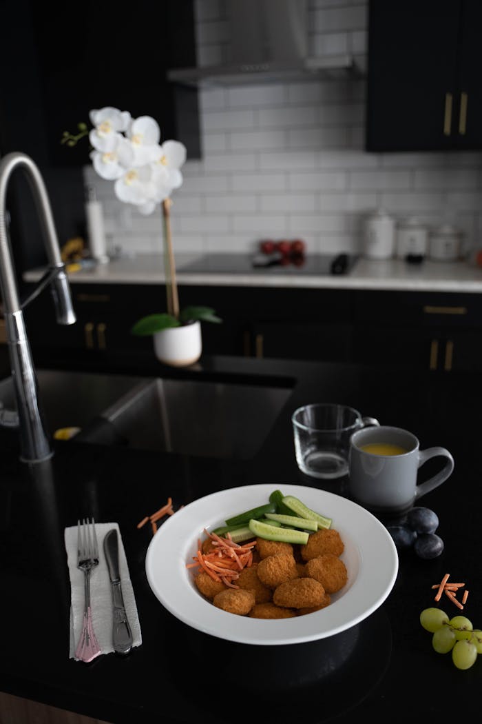 Stylish kitchen with a meal of nuggets, cucumber, and carrots on a black countertop.